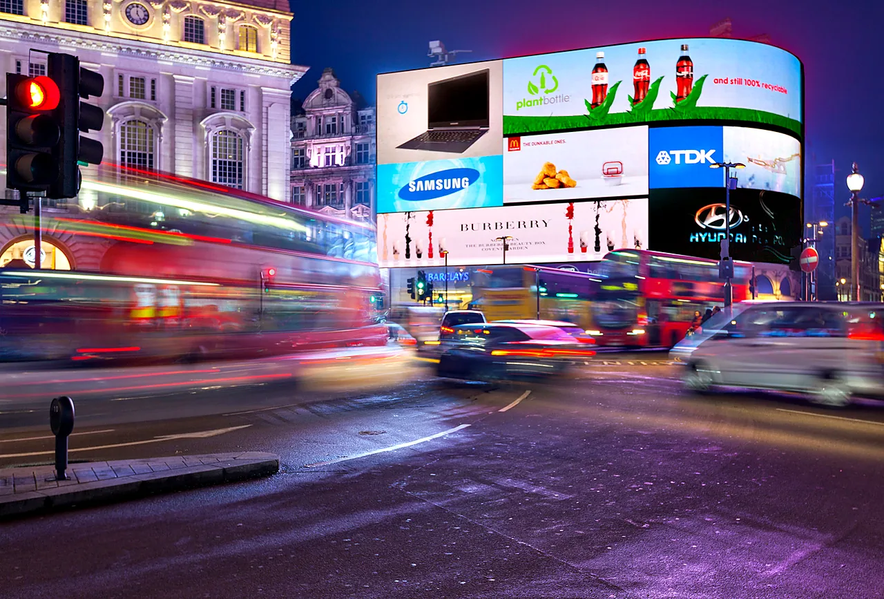Digital billboards above a busy city junction at dusk